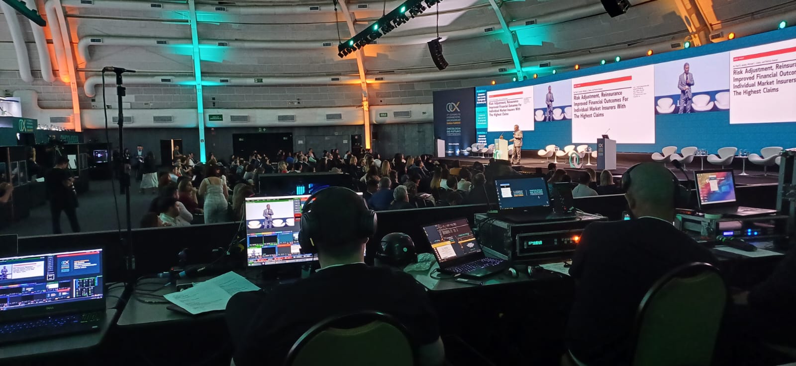 Operação de streaming e transmissão ao vivo do Grupo INAC, exibindo equipe técnica em mesa de corte e monitoramento de palco com grandes painéis de LED