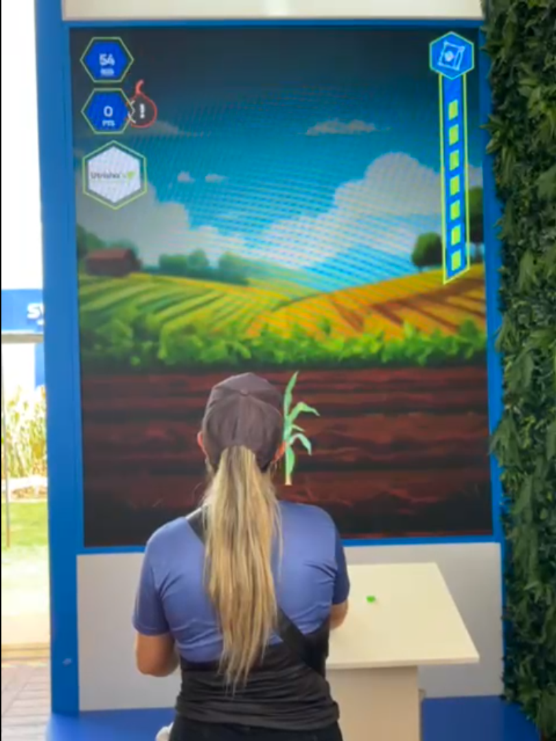 Participante interagindo com jogo digital personalizado sobre agronegócio em um grande painel de LED no stand de um evento, destacando gamificação para engajamento de público.
