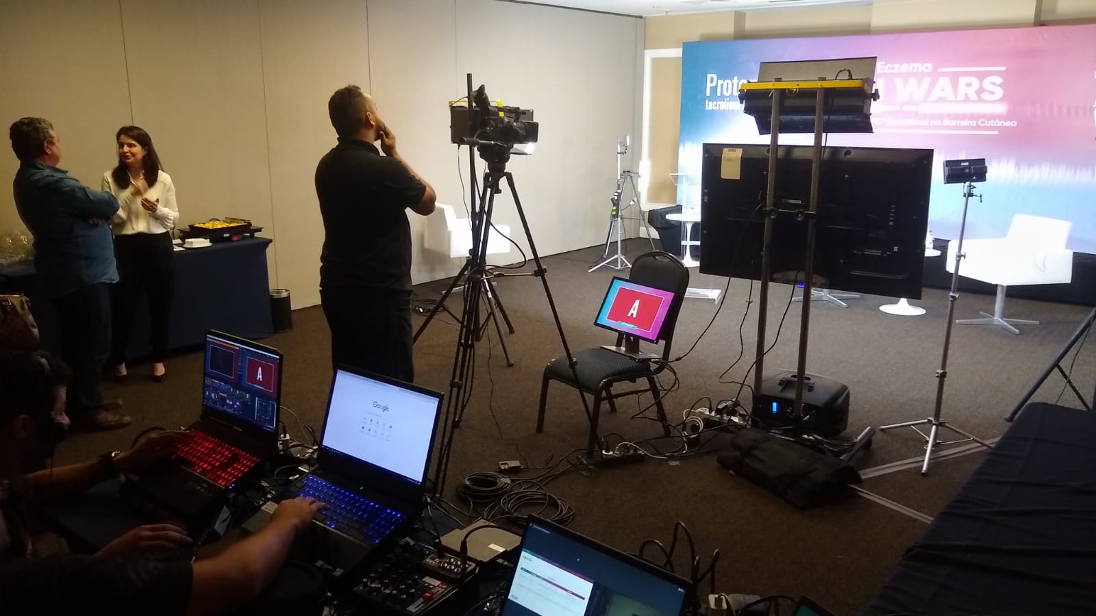 Bastidores de gravação audiovisual do Grupo INAC, com equipe operando câmeras em tripés, notebooks de monitoramento e iluminação profissional em estúdio para eventos corporativos.